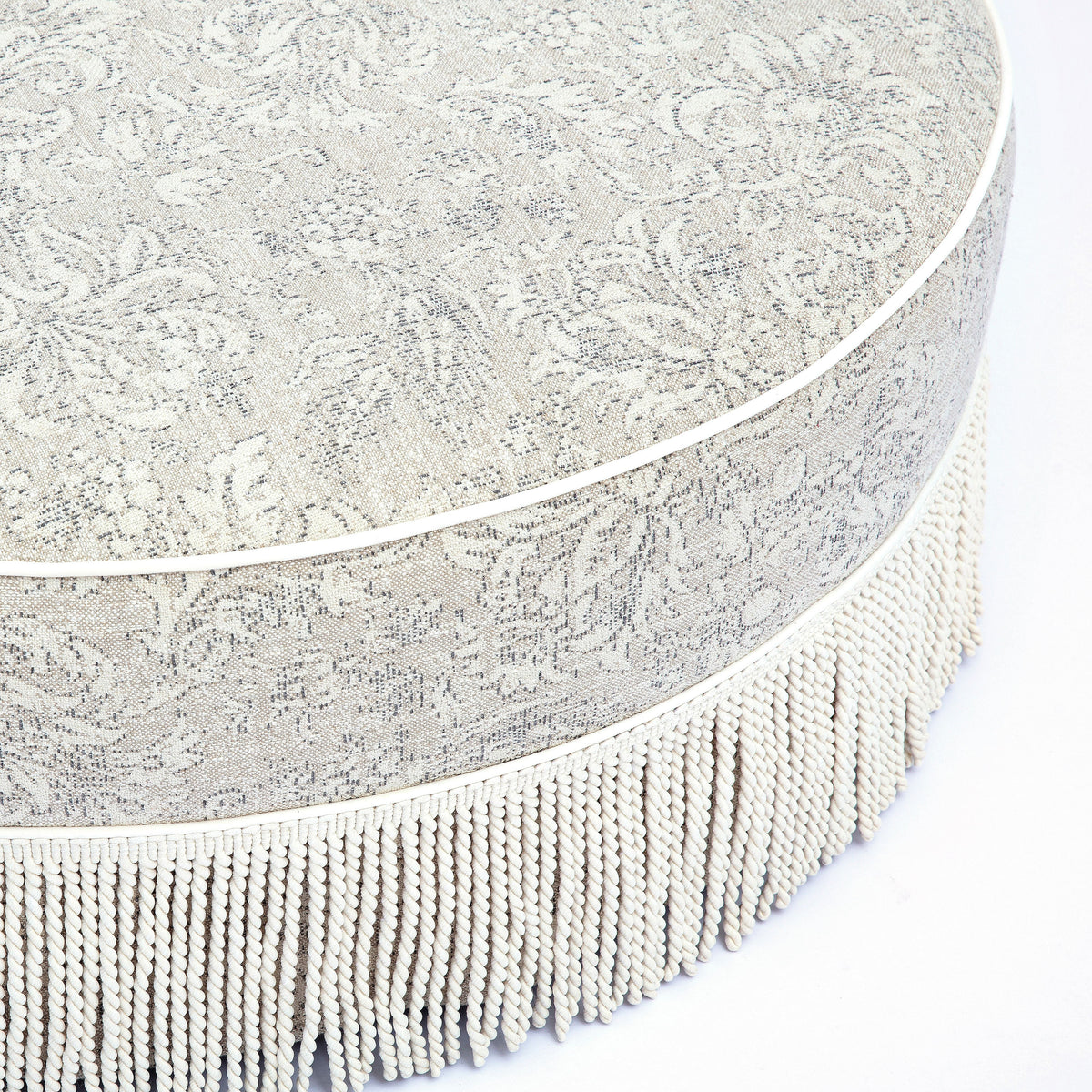 Tassy Tasseled Round Ottoman styled beside coffee table in contemporary seating area