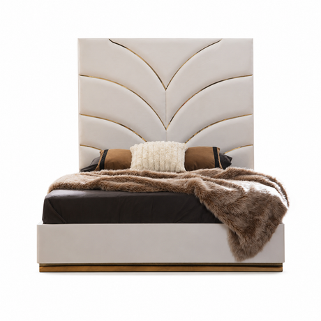 A modern upholstered bed with a tall segmented headboard in warm off-white, styled with dark bedding, a textured cream pillow, and a brown faux-fur throw blanket. The bed frame has a gold metal base trim, set against a plain white background.