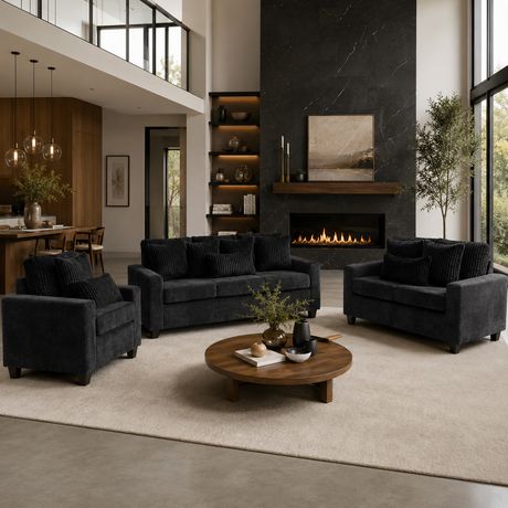 A modern living room featuring a dark charcoal gray three-piece sofa set (loveseat, armchair, and sofa) arranged around a round wooden coffee table on a large cream rug. The background showcases a contemporary black marble fireplace wall, built-in shelves, and a high-ceilinged loft-style interior.