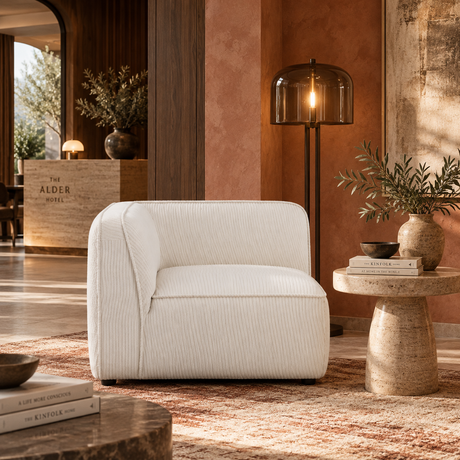 A modern off-white ribbed armchair in a warm, stylishly decorated living room with terracotta walls, a floor lamp, and a side table.