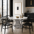 A round white marble dining table with a sculptural silver wire base, surrounded by four black wooden chairs in a modern kitchen setting.