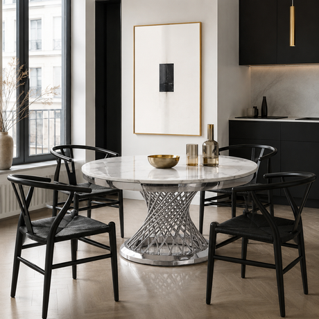 A round white marble dining table with a sculptural silver wire base, surrounded by four black wooden chairs in a modern kitchen setting.