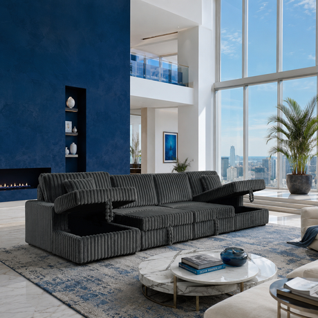 A modern sectional sofa in dark gray ribbed fabric, styled in a high-rise loft apartment with a blue accent wall, marble coffee table, and large windows overlooking a city skyline.