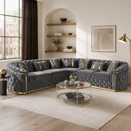 A luxury curved gray velvet sofa with gold trim and patterned accent pillows, styled in a modern living room with a glass coffee table and neutral rug.