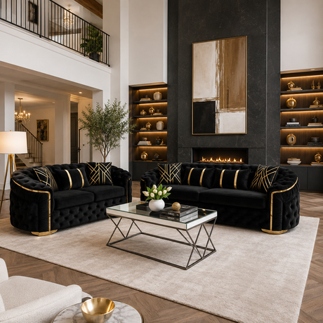 A luxury modern living room featuring two black tufted velvet sofas with gold trim and striped pillows, arranged around a glass-top coffee table on a large beige rug. The background includes a black fireplace wall, built-in shelves with warm lighting, and a high-ceilinged staircase.
