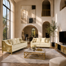 A luxury living room featuring a cream-colored sofa and matching armchair with ornate gold metal frames, styled with patterned pillows on a large gray rug. The room has high arched ceilings, warm beige walls, a marble coffee table with gold legs, and a flat-screen TV on a matching gold media console.