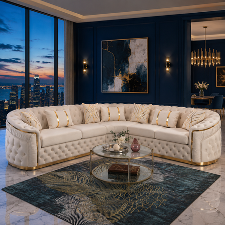 A luxurious curved tufted sofa upholstered in cream leather with gold trim, arranged in a U-shape in a modern living room with dark navy walls, a large abstract painting, and a glass coffee table.