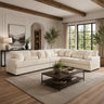 A large cream sectional sofa in a modern, sunlit living room with wood ceiling beams, a dark wood coffee table, and a textured beige rug.