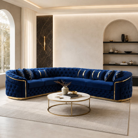 A luxurious curved tufted sofa upholstered in deep navy blue fabric with metallic gold trim, styled in a modern, elegant living room with a matching gold coffee table and neutral beige walls.
