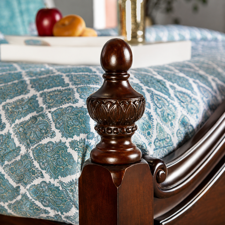 Close-up of a dark brown wooden bed post with a decorative finial, set against a blue and white patterned bedding and a softly blurred bedroom background.