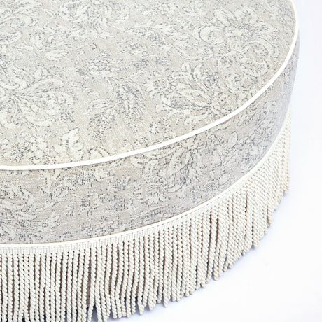 Tassy Tasseled Round Ottoman styled beside coffee table in contemporary seating area