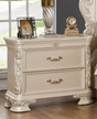 An ornate cream-colored two-drawer nightstand or end table with carved details and gold-toned handles, shown in a bedroom setting with decorative items on top.