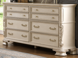 An eight-drawer dresser in a distressed cream or off-white finish with ornate silver metal handles and decorative carved side details, shown in a room setting with a wood floor and window.