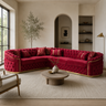 A luxurious curved tufted sofa upholstered in rich red velvet with gold trim, styled in a modern, warm-toned living room with a round wooden coffee table and neutral walls.